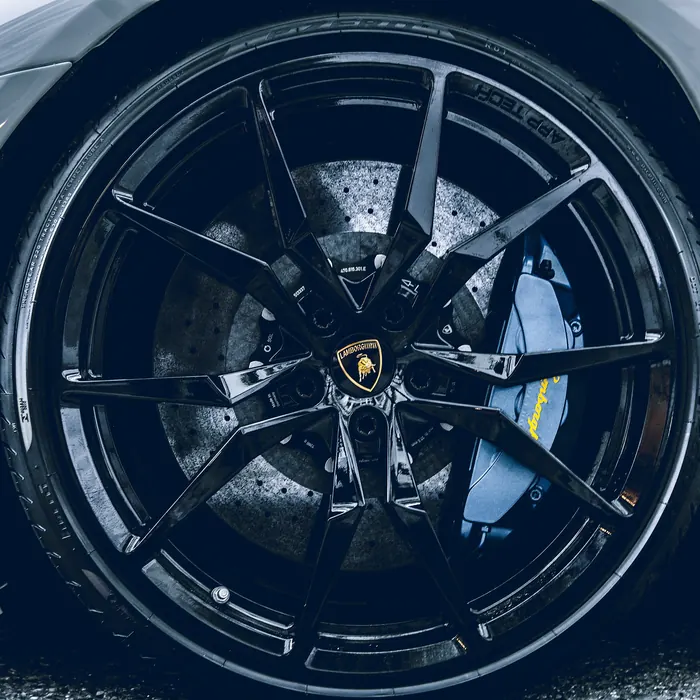 Gloss black wheel with a blue brake caliper on a white sports car