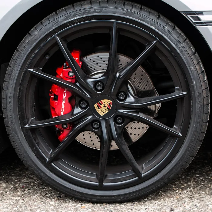 Flat black ten-spoke wheel with a red brake caliper on a silver Porsche