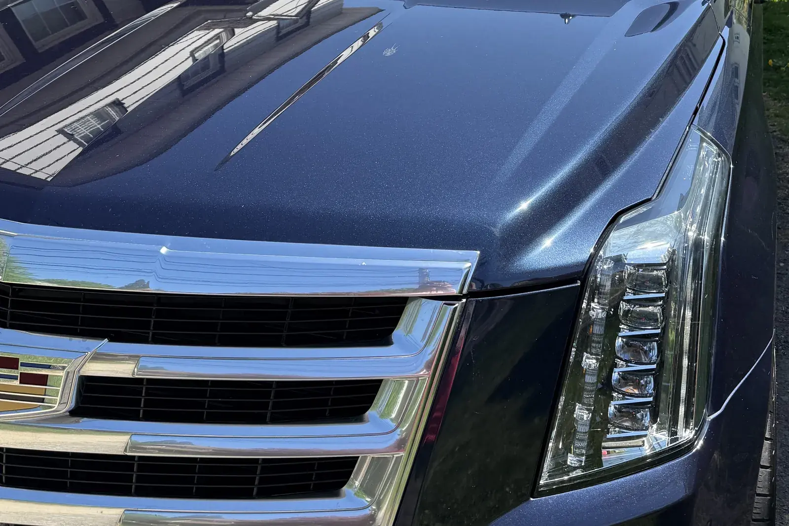 Front of a dark blue Cadillac Escalade: chrome grille and clear LED headlight