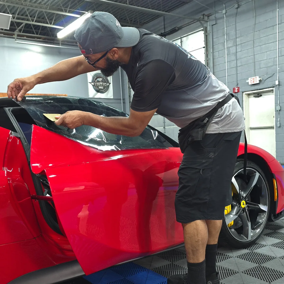 Jay fitting window film on the door glass of a red Ferrari in the Tint IQ 360 shop