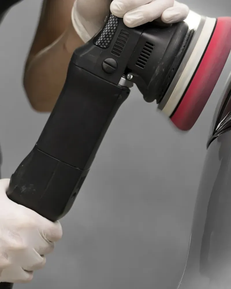 Machine polisher with a foam pad working the paint on a silver car